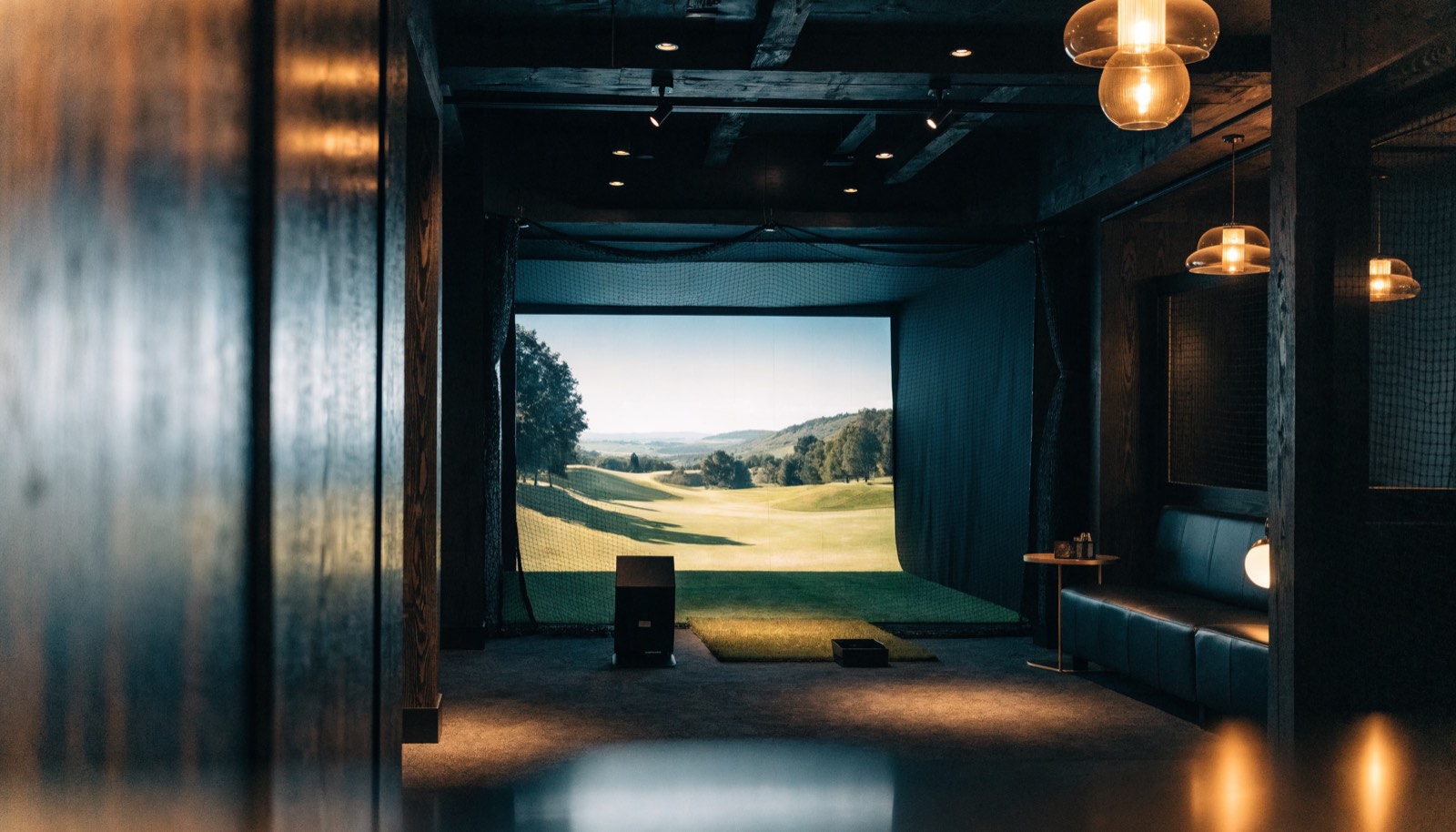 An indoor simulator bay with a course on the impact screen and a launch monitor on the floor