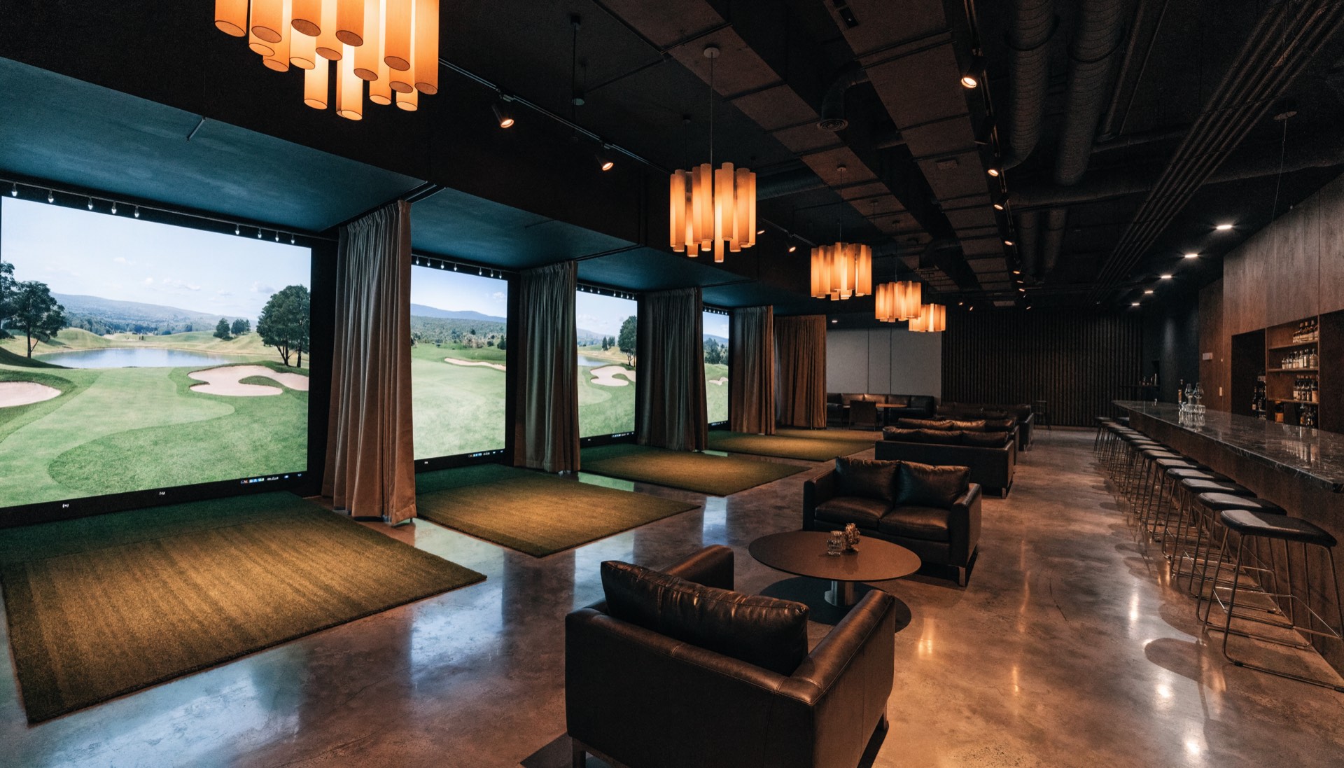 A row of indoor golf simulator bays with impact screens and a bar alongside